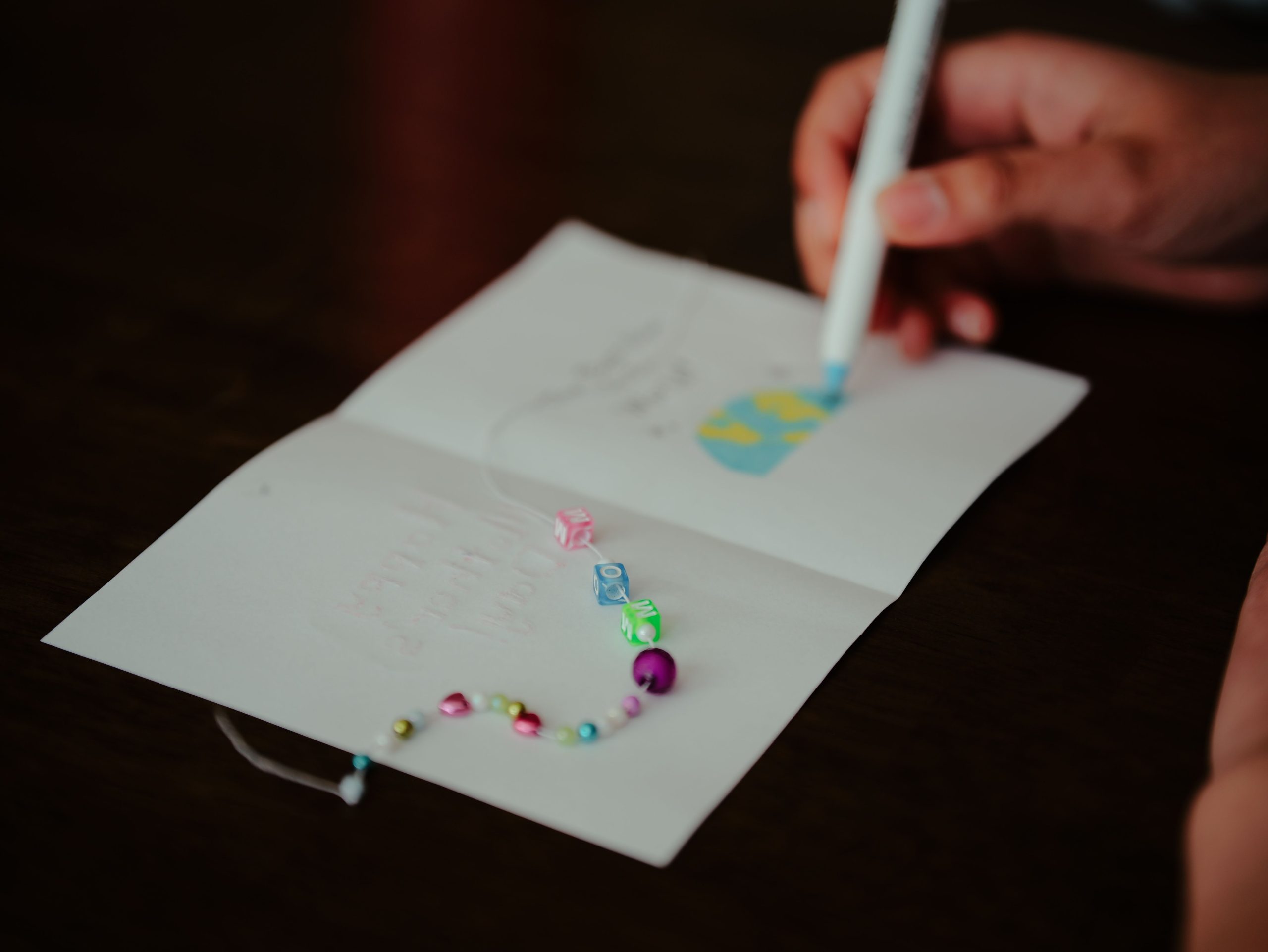 Hand decorating a greeting card with colorful beads and a pen for a personalized design